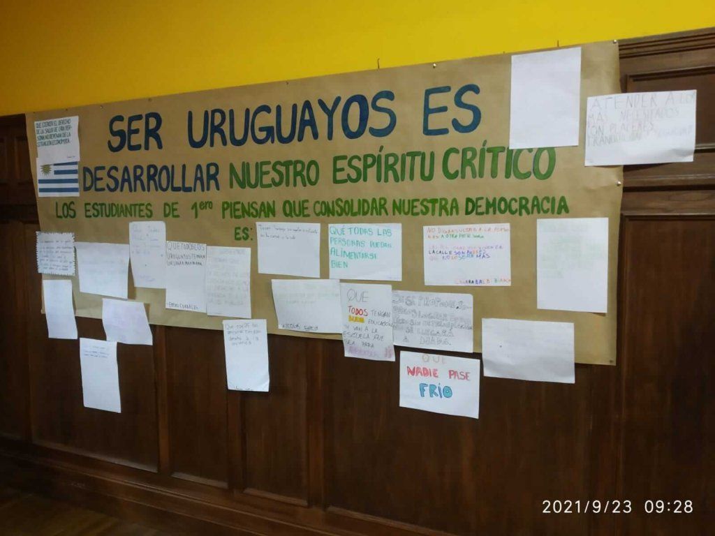 Cartel que dice: "Ser uruguayos es desarrollar nuestro espíritu crítico. Los estudiantes del 1.° piensan que consolidar nuestra democracia es:" con más carteles debajo.